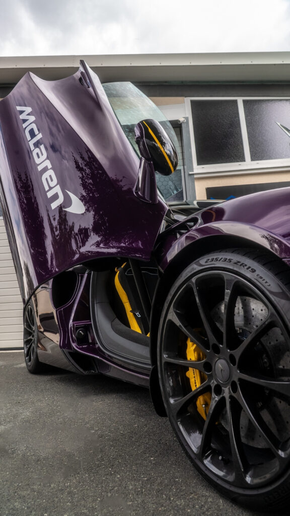 Ein Schriftzug McLaren ist auf einer offenen Flügeltüre eines hochprofessionell folierten Supersportwagen zu sehen. Die Farbe ist lila. Sauber und akurat angebracht an der linken hinteren Seitenscheibe eines Fahrzeugs.